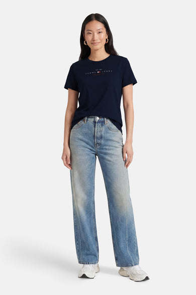 Donkerblauwe korte mouwen T-shirt van TOMMY JEANS met wit logo op borst, gedragen met lichtblauwe jeans en witte sneakers, front view.