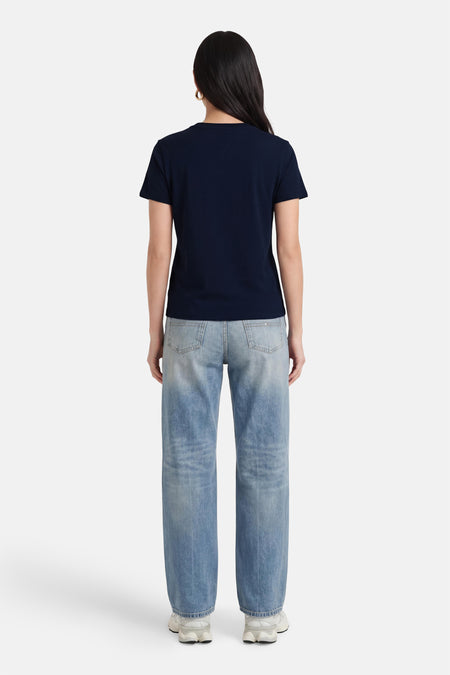 Donkerblauwe korte mouwen T-shirt van TOMMY JEANS, achterzijde weergegeven, gladde stof, model draagt lichtblauwe jeans en witte sneakers