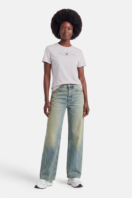 Grijze korte mouw T-shirt van TOMMY JEANS met klein logo op borst, gedragen met wijde jeans en witte sneakers, front view.