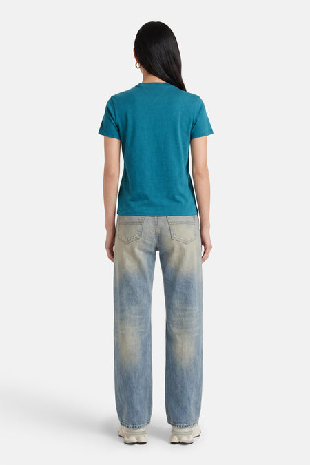 Groene korte mouwen t-shirt van TOMMY JEANS, achterzijde, gestreept denim broek, witte sneakers, model met donker haar