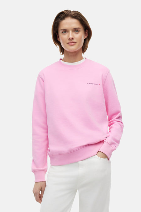 Pull rose à col rond de TOMMY JEANS avec logo rouge 'tommy jeans' sur la poitrine et drapeau sur la manche, porté par un mannequin.