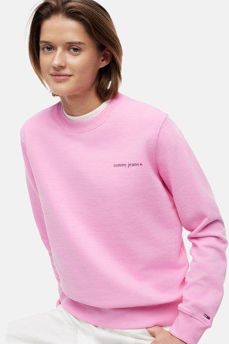 Roze ronde hals sweater van TOMMY JEANS met rood 'tommy jeans' logo op de borst en vlag op de mouw, gedragen door een model.