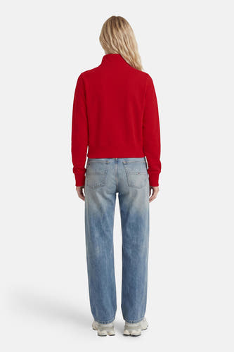 Rode ronde hals sweater van TOMMY JEANS, achterkant, met ribboorden en strakke pasvorm, gedragen met lichtblauwe jeans en witte sneakers.