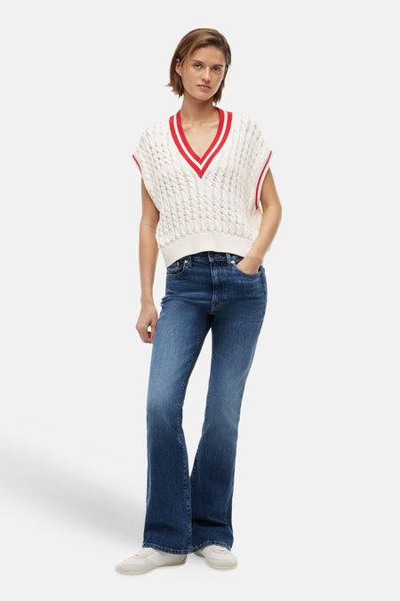 Débardeur en maille écru de TOMMY JEANS avec des rayures rouges et blanches sur l'encolure en V et un motif torsadé, porté avec un jean bleu et des baskets blanches.
