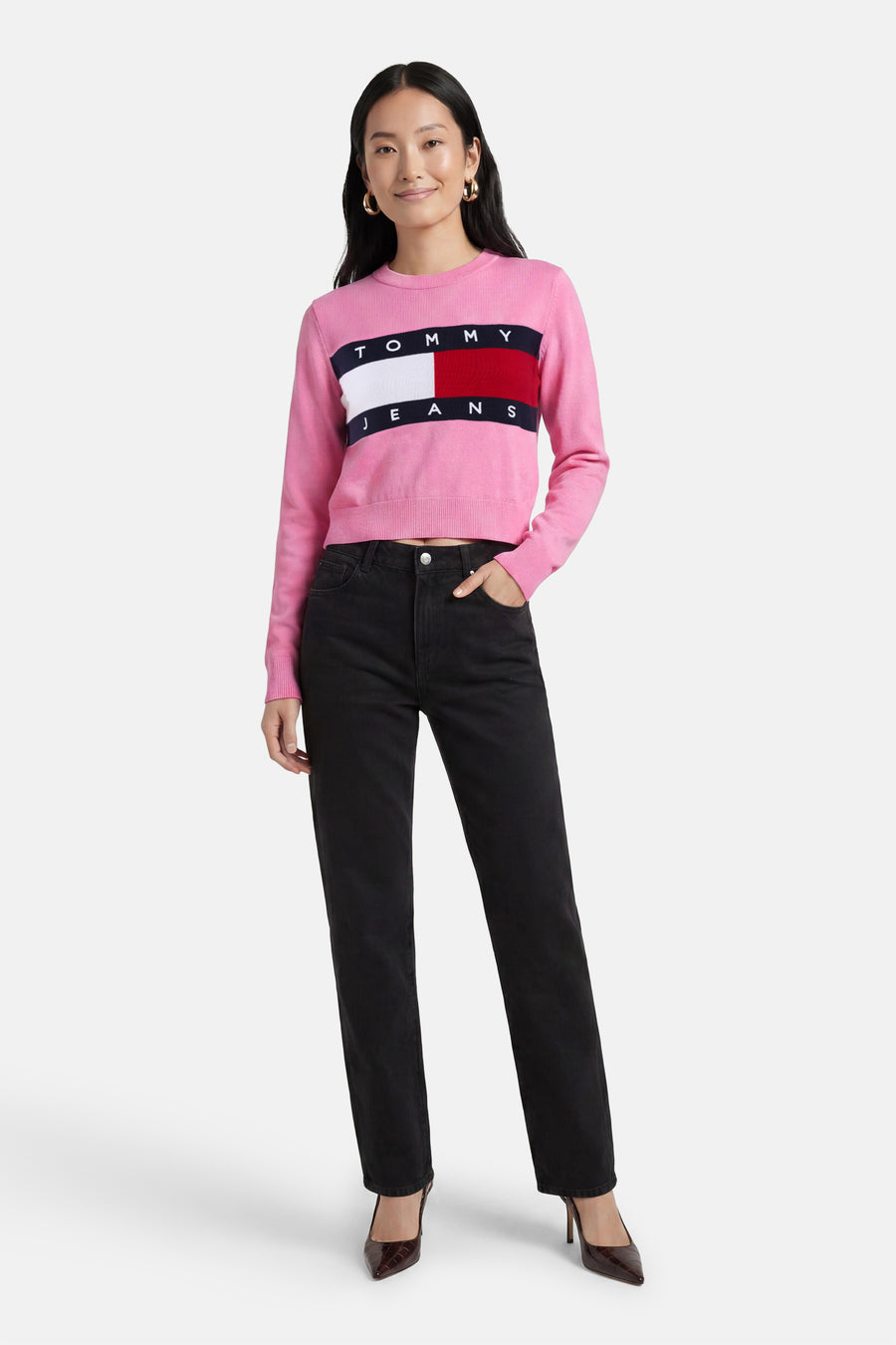 Roze ronde hals trui met Tommy Jeans logo band, van TOMMY JEANS, gedragen met zwarte jeans en bruine hakken, front view