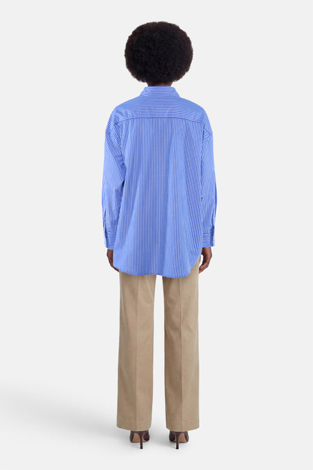 Blauw gestreept overhemd met lange mouwen van TOMMY JEANS, achterkant, losse pasvorm, witte strepen, model draagt beige broek en hoge hakken