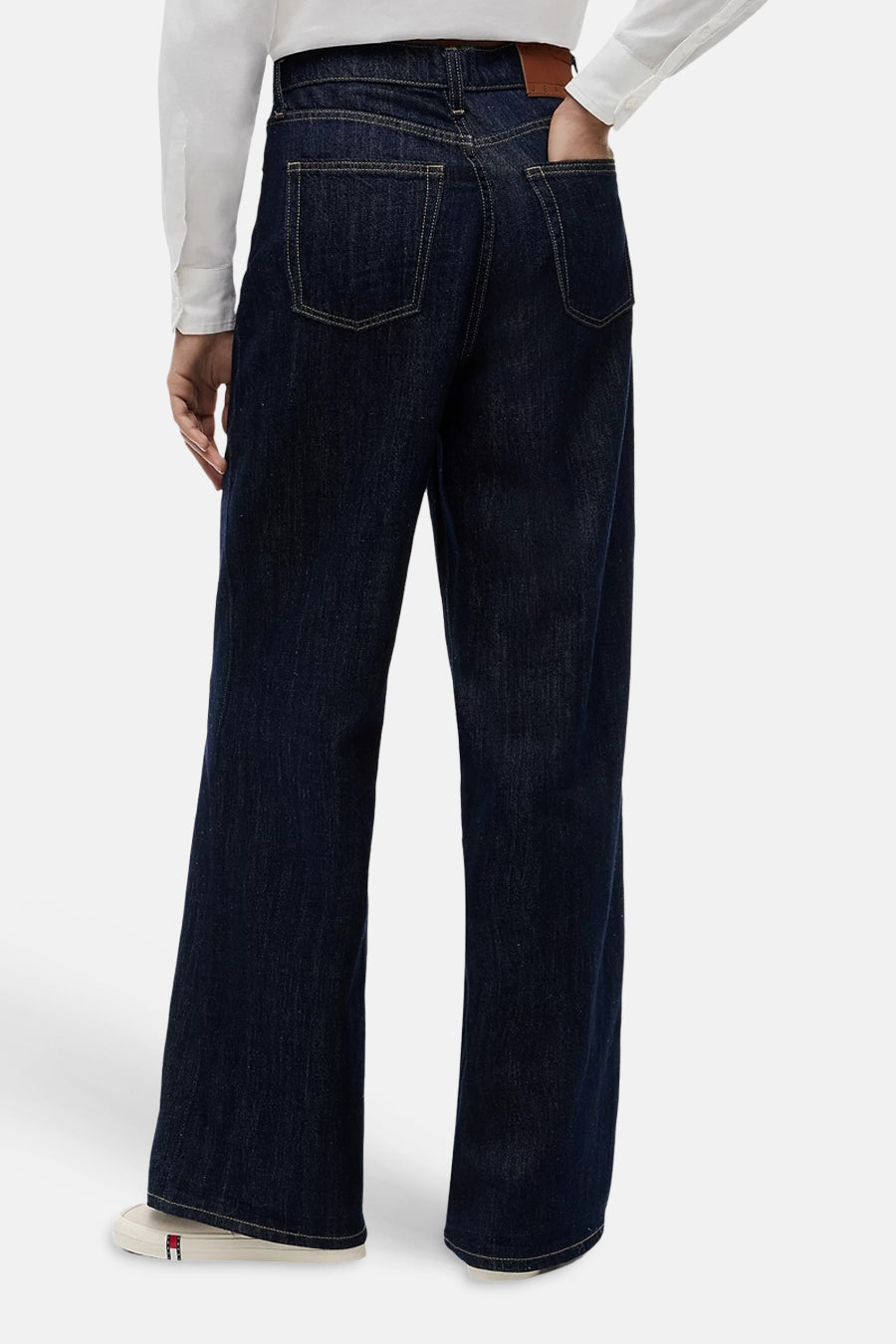 Donkere blauwe wijde jeans van TOMMY JEANS, achterzijde, met contrasterende naden en bruin label, gedragen met wit overhemd en witte sneakers
