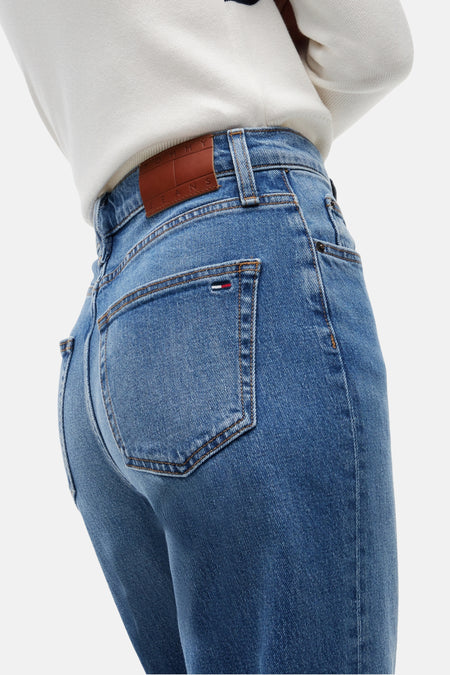 Midblauwe straight jeans van TOMMY JEANS, achterzijde met bruin label en kleurrijke vlag op achterzak, gedragen met witte trui