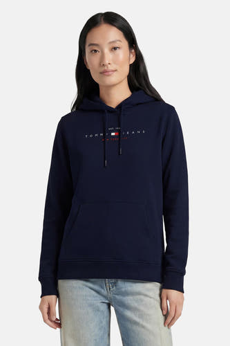 Donkerblauwe sweater met kap van TOMMY JEANS, voorzien van logo op borst, zakken en trekkoord, gedragen met lichtblauwe jeans.