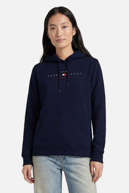 Donkerblauwe sweater met kap van TOMMY JEANS, voorzien van logo op borst, zakken en trekkoord, gedragen met lichtblauwe jeans.