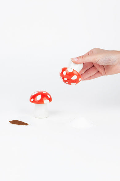 Rode paddenstoel peper- en zoutstel van DOIY, met witte stippen, met een hand die schudt op een witte achtergrond.
