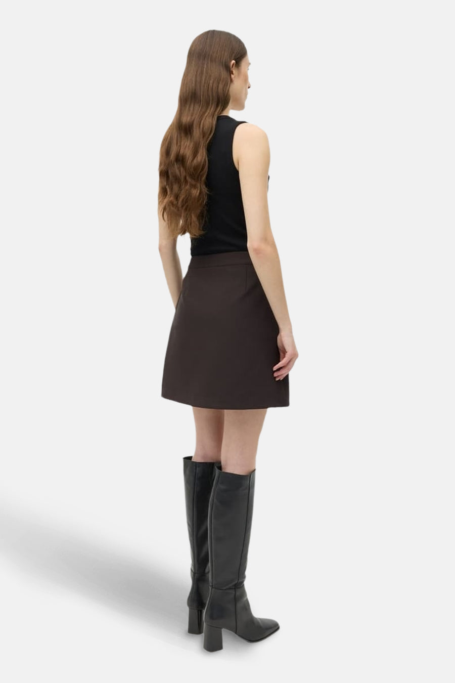 Vrouw in zwarte top, bruine rok en zwarte leren laarzen.