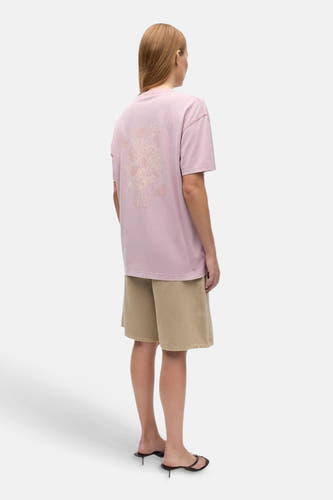 Roze T-shirt van ENVII met ton-sur-ton bloemenprint op de rug, gecombineerd met kaki shorts en zwarte sandalen.
