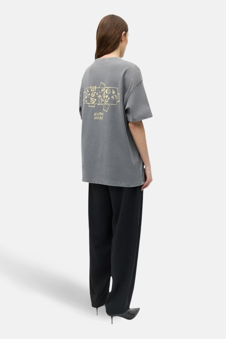 T-shirt gris à manches courtes ENVII, avec imprimé graphique au dos, combiné avec un pantalon noir et des escarpins.