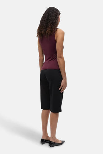 Bordeaux top zonder mouwen van ENVII, met krullend haar en zwarte broek.
