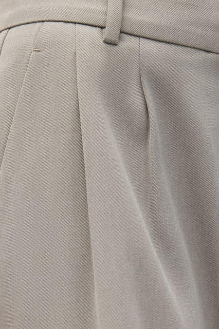 Pantalon beige d'ENVII, avec des plis et un détail de passant de ceinture.