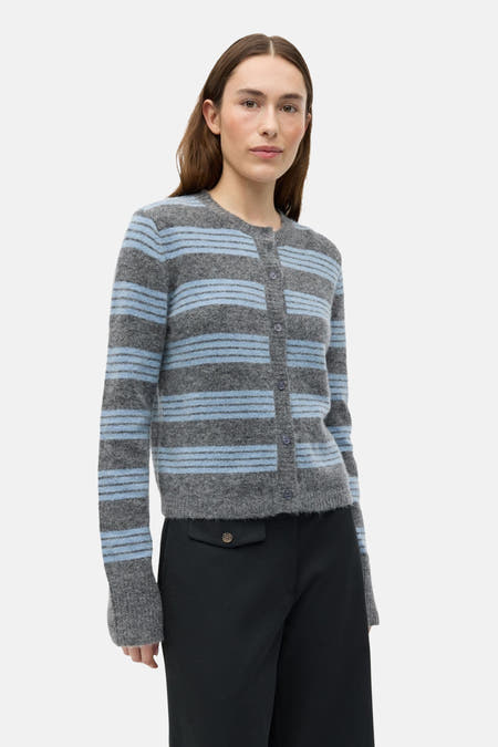 Grijs gilet van ENVII, met blauwe strepen en lange mouwen, gedragen met een zwarte broek.
