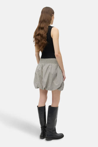 Korte beige rok van ENVII, met een geruit patroon en gecombineerd met zwarte laarzen en top.