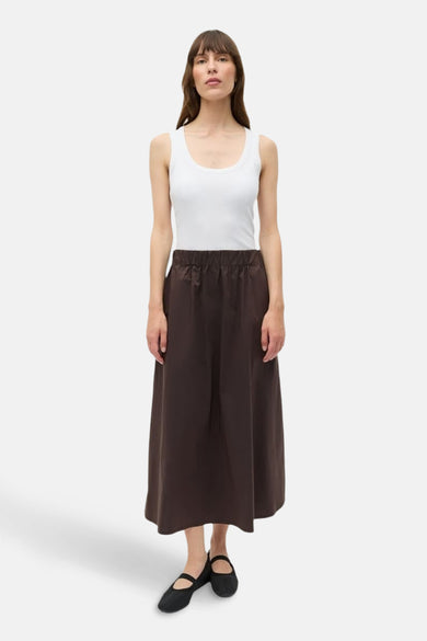 Jupe brune d'ENVII, associée à un tank-top blanc et des ballerinas noires.