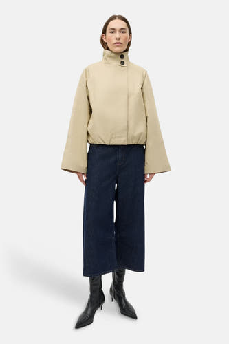 Manteau court beige d'ENVII à manches longues, col montant et boutons noirs, associé à un jean foncé et des bottes noires.
