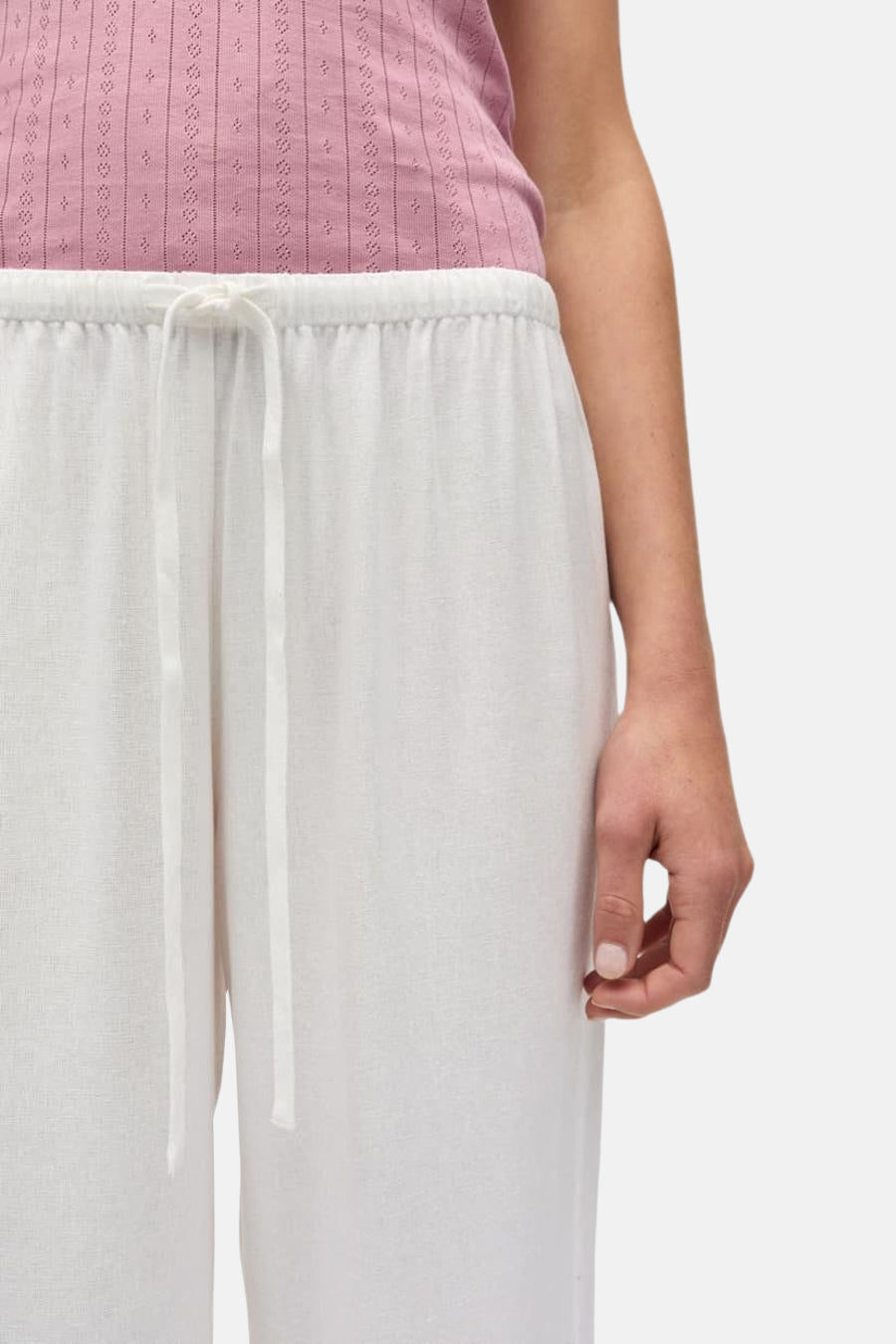 Witte broek van ENVII met trekkoord in de taille, lichte linnen textuur en een deel van een roze top.