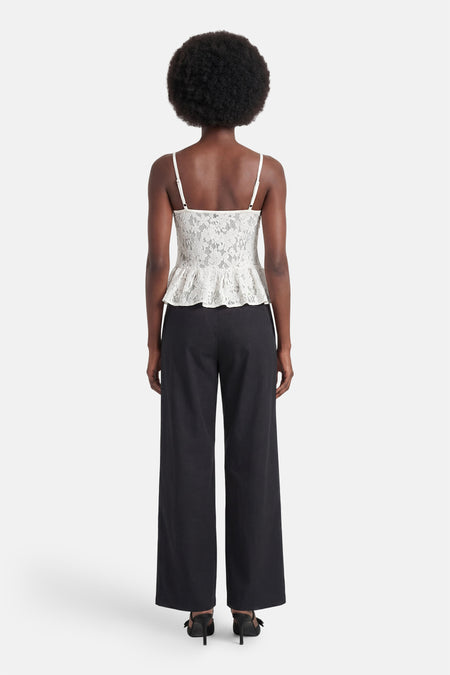 Chemisier blanc sans manches en dentelle d'ENVII avec bretelles spaghetti et ourlet péplum, porté avec un pantalon noir et des mules, vue arrière.