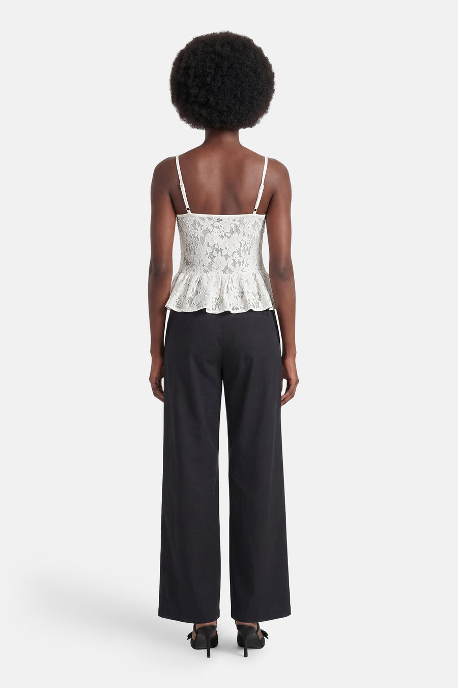 Witte mouwloze kanten blouse van ENVII met spaghettibandjes en peplumzoom, gedragen met zwarte broek en muiltjes, achteraanzicht.
