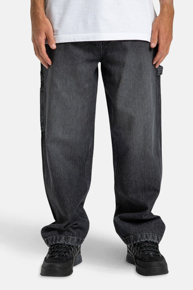 Donkergrijze denim jeans wide van DC SHOES, met gereedschapszakken, gecombineerd met zwarte sneakers en een wit T-shirt.