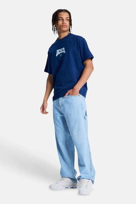 Lichtblauwe denim jeans met speciale pasvorm van DC SHOES, met utility-zak, gedragen met een donkerblauw T-shirt en witte sneakers.