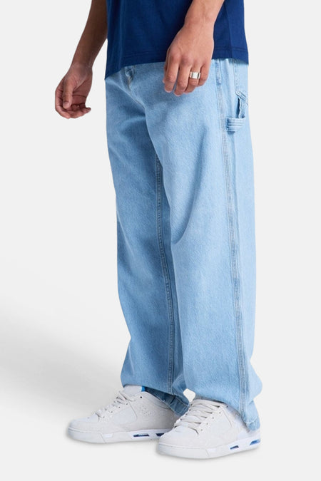 Lichtblauwe denim jeans met speciale pasvorm van DC SHOES, met wijde pijpen, gereedschapslus, witte sneakers en zilveren ring.