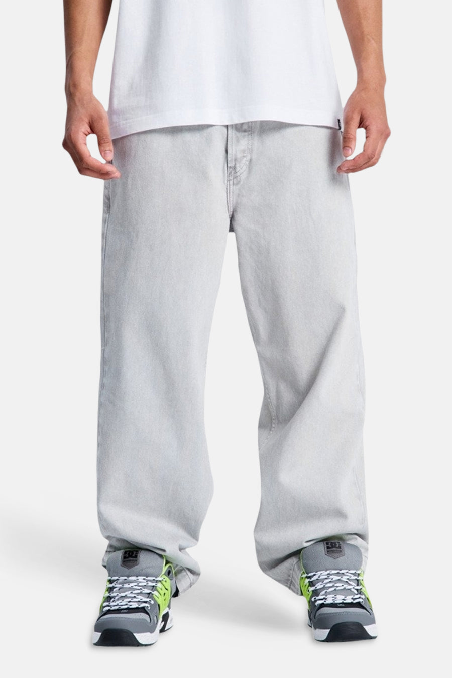 Lichtgrijze denim jeans met speciale pasvorm van DC SHOES, gedragen door een persoon met een wit t-shirt en grijze sneakers met neon details.