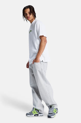 Jeans in lichtgrijs denim van DC SHOES met losse pasvorm, gedragen door model met wit T-shirt en neon sneakers.