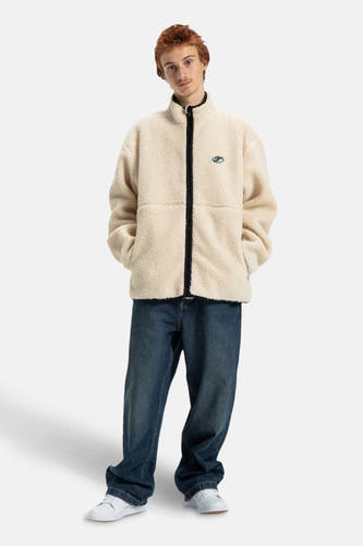 Beige korte jas van DC SHOES, met lange mouwen en gedragen met een blauwe jeans en witte schoenen.