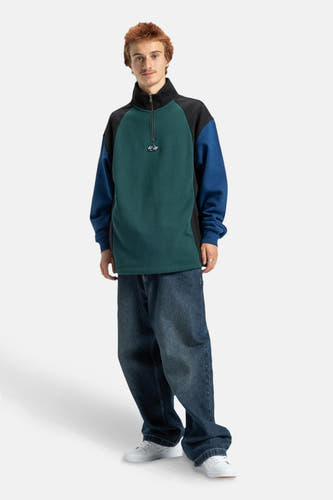 Sweater multicolore de DC SHOES, avec une fermeture éclair mi-longue, des manches longues et associé à des jeans décontractés et des baskets blanches.