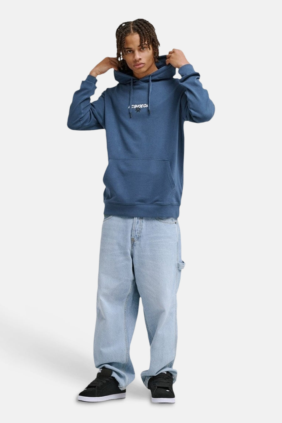 Blauwe sweater met kap van DC Shoes, met trekkoorden en een buidelzak. De man draagt wijde jeans en zwarte schoenen.