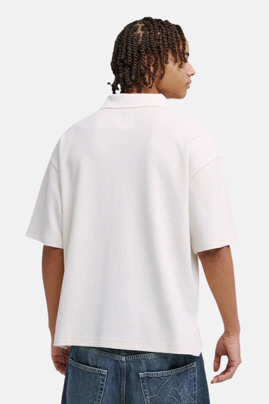 Witte oversized polo van DC SHOES met lichte textuur, achteraanzicht. Model met vlechten en jeans.