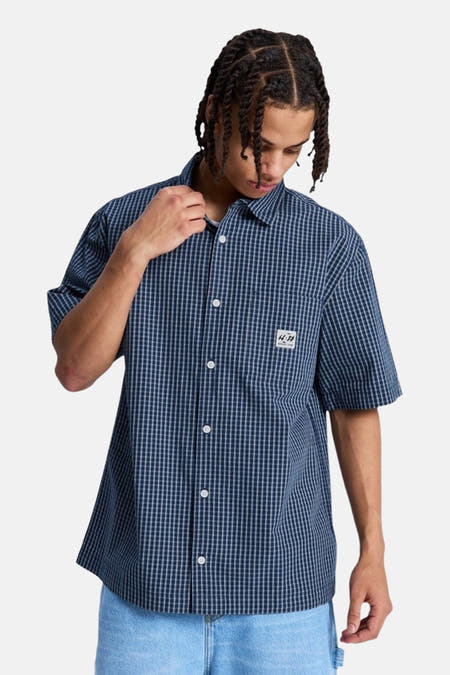 Blauw geruit hemd met korte mouwen van DC SHOES, met borstzakje en wit label, gedragen door een man.