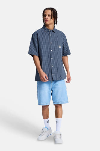 Blauw geruit hemd met korte mouwen van DC SHOES, gedragen door een man met denim shorts en sneakers.