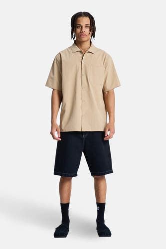 Chemise marron à manches courtes de DC SHOES, avec fermeture boutonnée et poche poitrine, associée à un short en jean, des chaussettes et des mocassins.