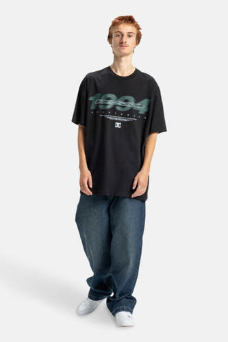 T-shirt noir à manches courtes de DC SHOES, avec un imprimé sur la partie avant et porté avec des jeans larges et des baskets blanches.