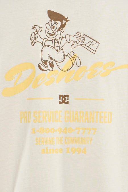 Beige T-shirt van DC SHOES met een tekening van een timmerman en gele tekst.

