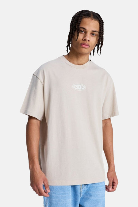 T-shirt beige ample à manches courtes de DC SHOES avec logo ovale blanc DC SHOE CO sur la poitrine.