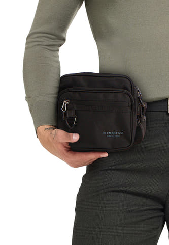 Sac à dos noir d'Element, avec des fermetures éclair discrètes et un logo discret, porté avec un pantalon large et une chemise verte.