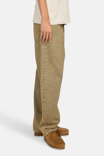 Wijd uitlopende off-white jeans van ELEMENT, met bruine schoenen en een beige T-shirt, in zijaanzicht.
