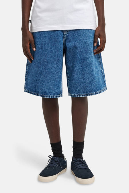 Denim jeansshort in middenblauw van ELEMENT, met wijde pijpen en gedragen met zwarte sokken en donkerblauwe schoenen.
