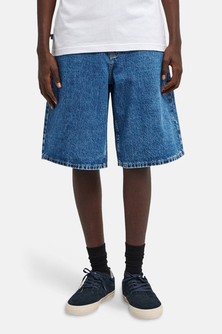 Denim jeansshort in middenblauw van ELEMENT, met wijde pijpen en gedragen met zwarte sokken en donkerblauwe schoenen.
