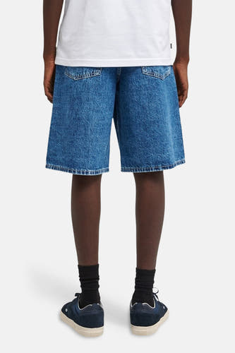 Jeansshort van ELEMENT, in middenblauw denim, met achterzakken en gecombineerd met zwarte sokken en blauwe schoenen.