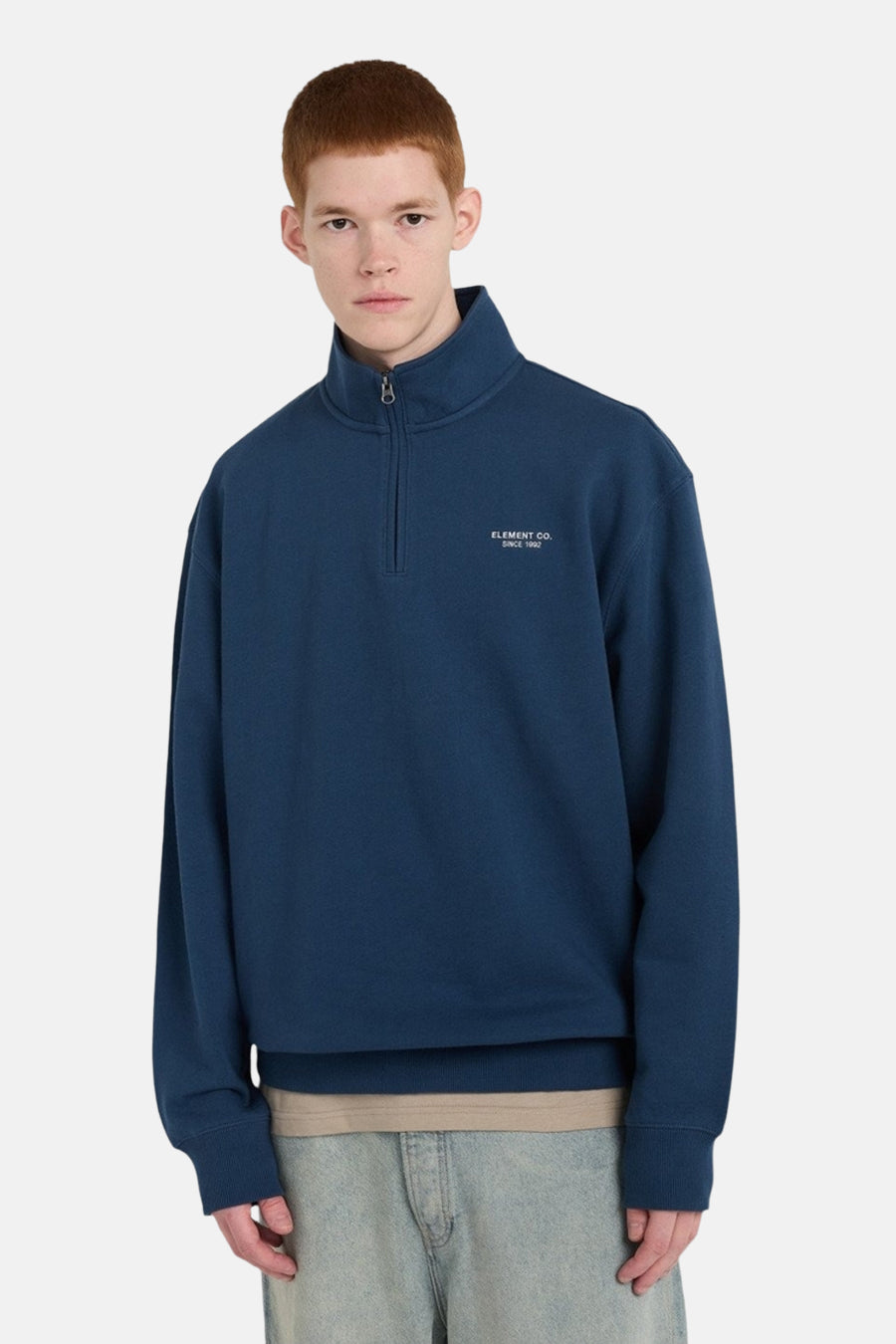 Blauwe sweater van ELEMENT, met korte ritssluiting en subtiele tekstprint op de borst, gedragen met een beige shirt en lichte jeans.
