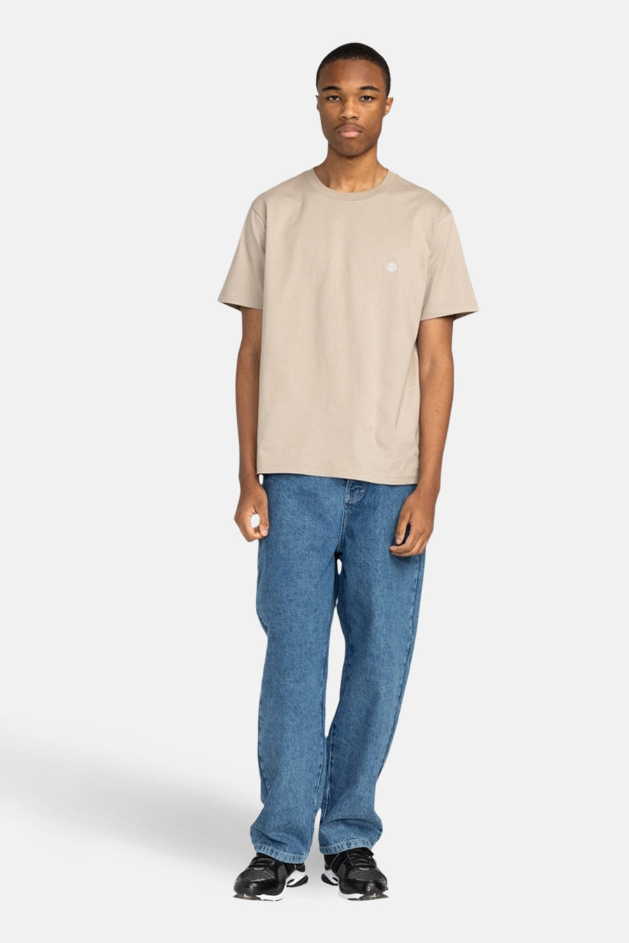 Beige T-shirt met korte mouwen van ELEMENT, gedragen met wijde blauwe jeans en zwarte sneakers.