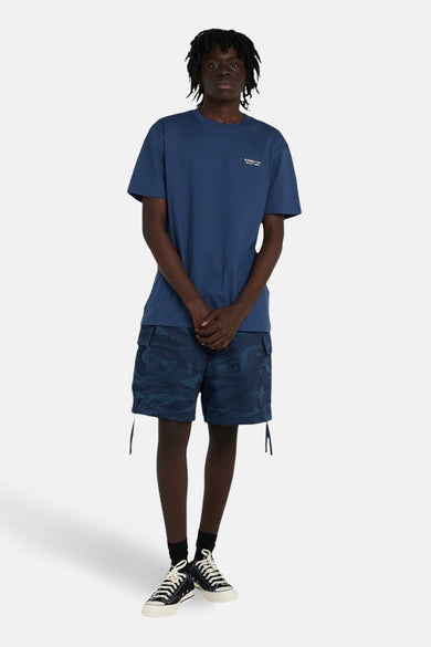T-shirt bleu à manches courtes d'ELEMENT, avec un petit texte sur la poitrine. Porté avec des shorts camouflage et des baskets noires.